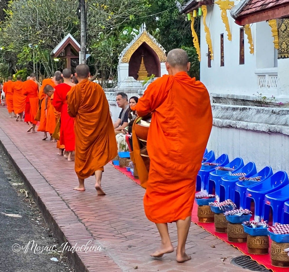 Morning alms ceremony in Luang Prabang, Laos, with Theravada Buddhist monks walking through the streets in traditional robes in the early morning hours