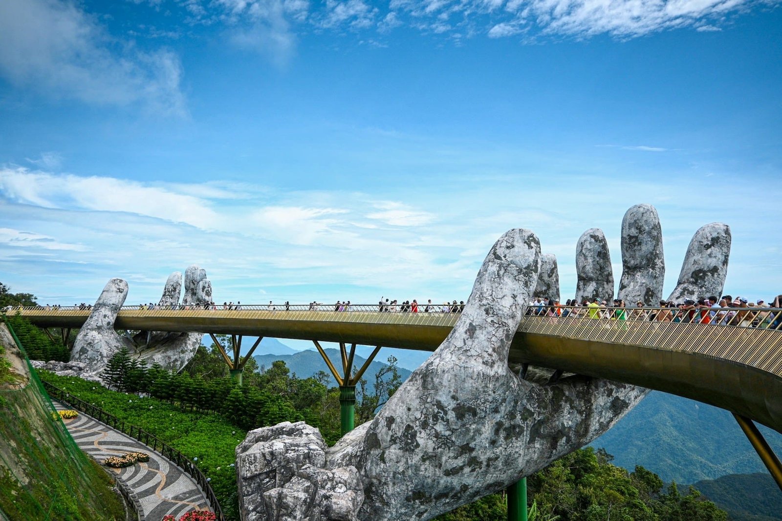 Golden Bridge at Ba Na Hills, Vietnam, held by giant stone hands amid scenic mountain views.