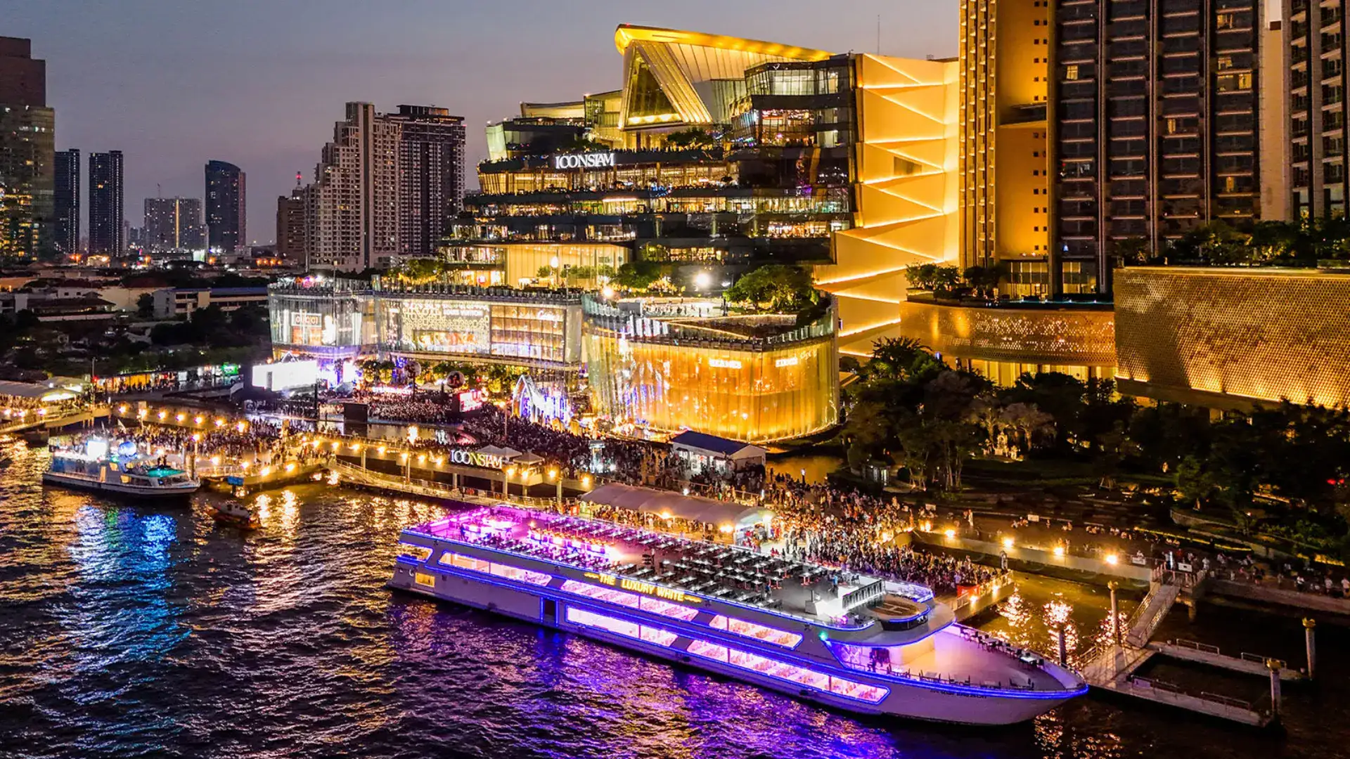 Evening view of ICONSIAM in Bangkok with bustling crowds and Chao Phraya River dinner cruises, a popular stop on Bangkok city tours.